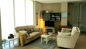 A living room with a sofa, armchair, coffee table, TV stand, and shelves with books and decorative items. - Beautiful 2-bed Apartment Near Waterford City (Waterford)