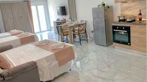 Una habitación de hotel moderna con dos camas, zona de comedor, cocina y un amplio ventanal.