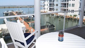 A balcony with a view of a marina, a white chair, and a table with a jar. - Sunset Bay Villa #210- Waterfront Condo in Town, Pool, Gym (Chincoteague)