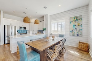 A modern kitchen with white cabinetry, a central island, and a dining area with a wooden table and wicker chairs.