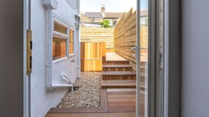 A narrow pathway leading to a wooden deck with steps, surrounded by a white wall and a wooden fence.