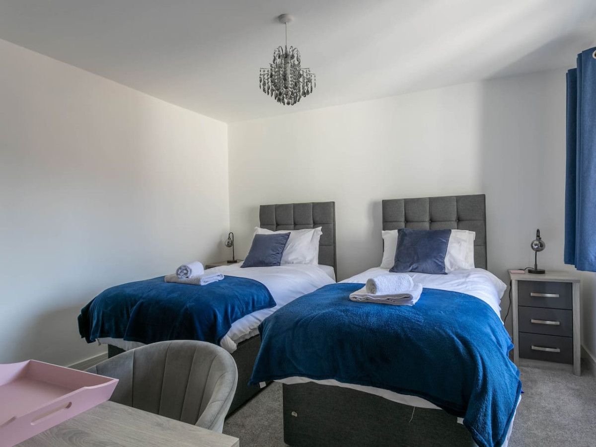 A hotel room with two beds, a desk, a chair, a nightstand, and a chandelier.