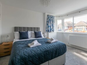 Een slaapkamer met een groot bed, een grijs hoofdeinde en uitzicht buiten door een raam.