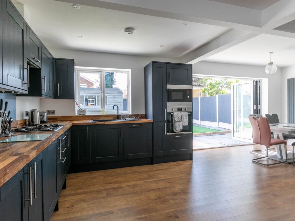 A modern kitchen with dark cabinetry, a wooden countertop, and a built-in oven.