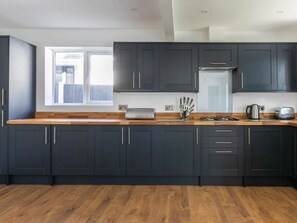 Une cuisine moderne avec des meubles de couleur sombre, un plan de travail en bois et une fenêtre qui laisse entrer la lumière naturelle.