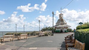 Eine Strandpromenade mit Bänken, einem Pavillon und Blick auf das Meer.