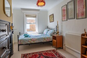 Ein Schlafzimmer mit Bett, Schminktisch, Heizkörper, Fenster und Bildern an der Wand.