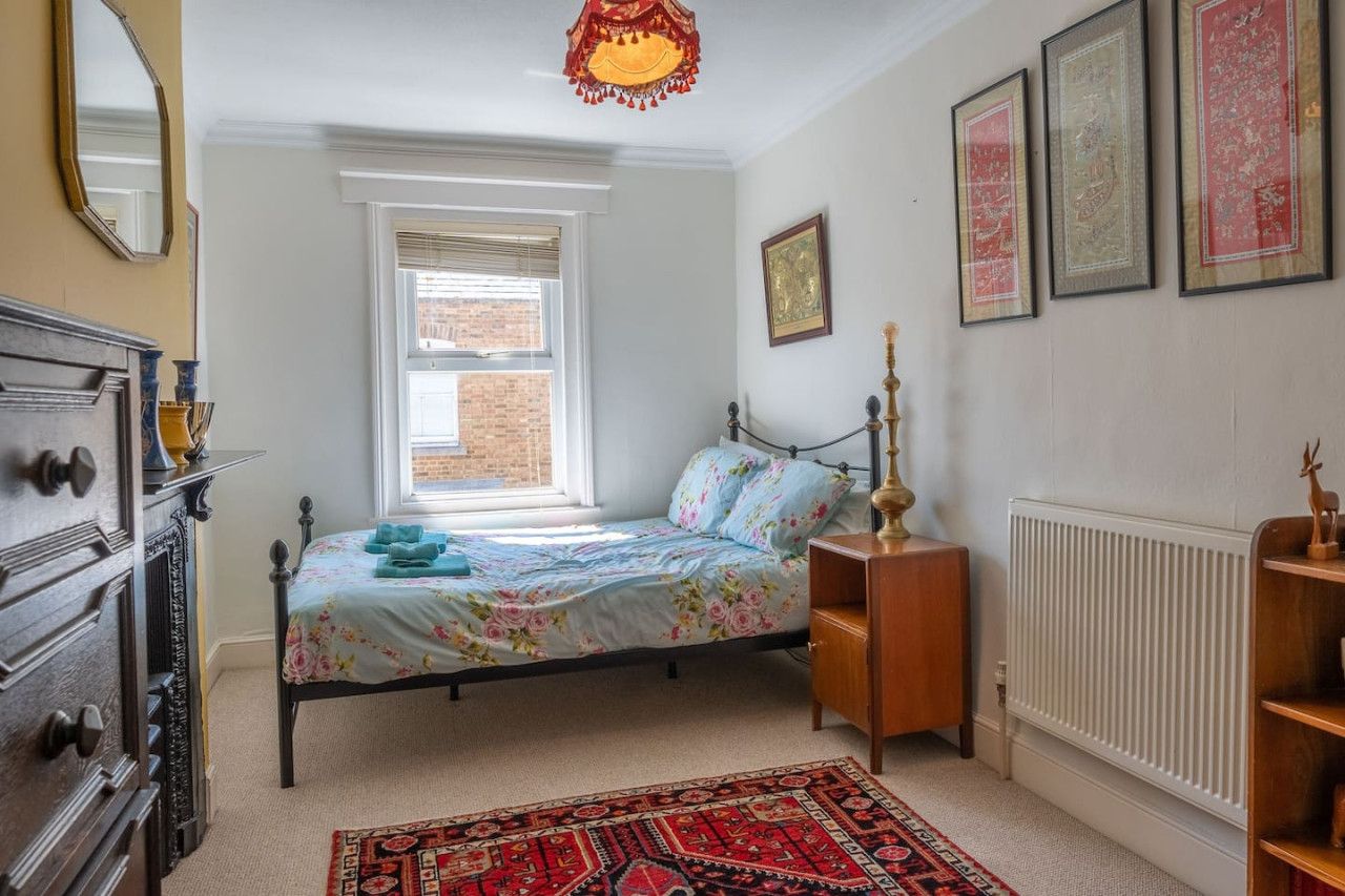A bedroom with a bed, dresser, radiator, window, and artwork on the wall.