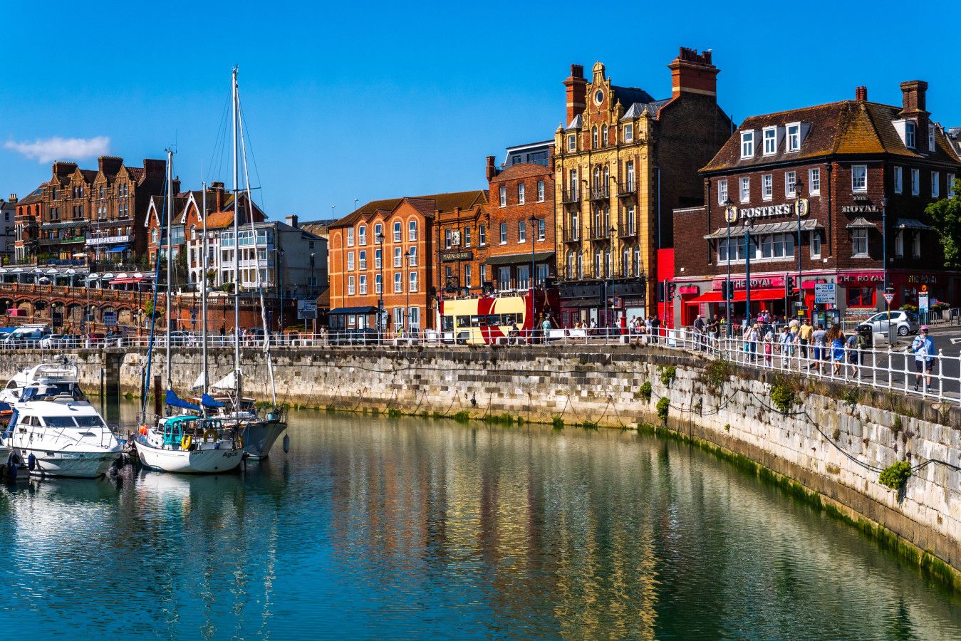 A waterfront area with historic buildings, a marina with boats, and a stone wall.
