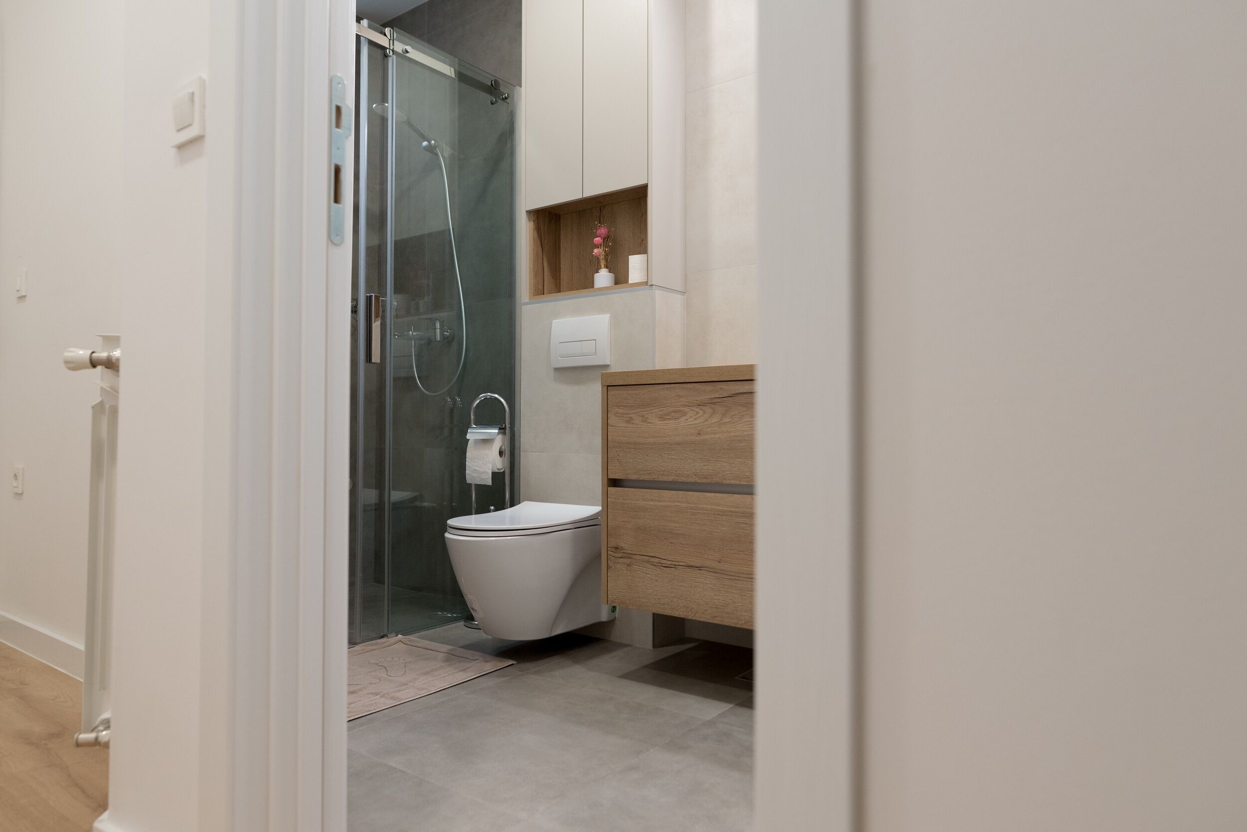 A modern bathroom with a glass shower enclosure, a white toilet, and a wooden vanity with a shelf.