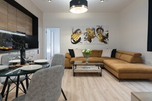 A modern living room with a glass dining table, grey chairs, a brown sectional sofa, and abstract wall art.