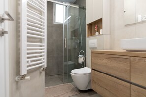A modern bathroom with a glass-enclosed shower, a white toilet, and wooden cabinetry.
