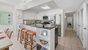 A modern kitchen with white cabinets, a central island with stools, a microwave, and a refrigerator.