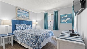 Un dormitorio con una cama, dos mesitas de noche, un escritorio, un televisor de pantalla plana y obras de arte en las paredes.