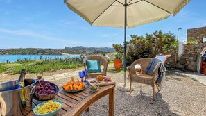 Una mesa al aire libre con vista al mar, una silla de mimbre y un muro de piedra.