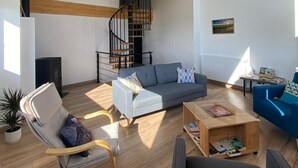 Ein geräumiges Wohnzimmer mit hohen Decken, Holzbalken, einer Wendeltreppe und einem großen Fenster für viel Tageslicht.