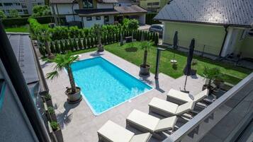 Ein rechteckiger Swimmingpool, umgeben von Liegestühlen und Topfpflanzen, mit Blick auf Nachbarhäuser und einen klaren Himmel.