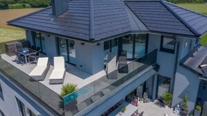 Una casa moderna con un amplio balcón de vidrio, un comedor y vistas a las montañas.