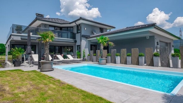 Una casa moderna de dos pisos con piscina, mobiliario exterior y plantas en macetas.
