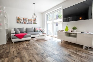 Una sala de estar moderna con un sofá gris, un mueble de TV blanco y una televisión grande.