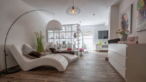 Ein modernes Wohnzimmer mit einer gebogenen Couch, einer großen Stehlampe und einem Glastregal.