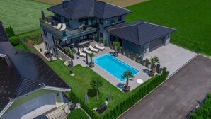 Ein modernes, zweigeschossiges Haus mit Swimmingpool, Sitzgelegenheiten im Freien und einem gepflegten Rasen.