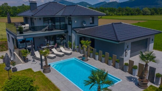 Ein modernes, zweistöckiges Haus mit Pool, Sitzgelegenheiten im Freien und Bergblick.
