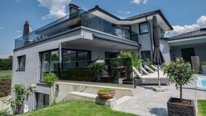 Ein modernes, zweistöckiges Haus mit Glasbalkon, Sitzbereich im Freien und einem Swimmingpool.
