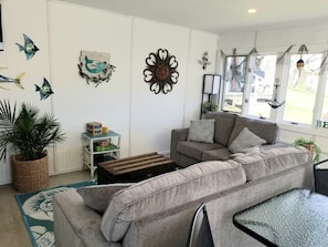 A living room with a grey sofa, a small wooden table, a woven basket, and a potted plant. - Spacious yet cozy, newly remodeled home steps away from the Surf Ballroom. (Clear Lake)