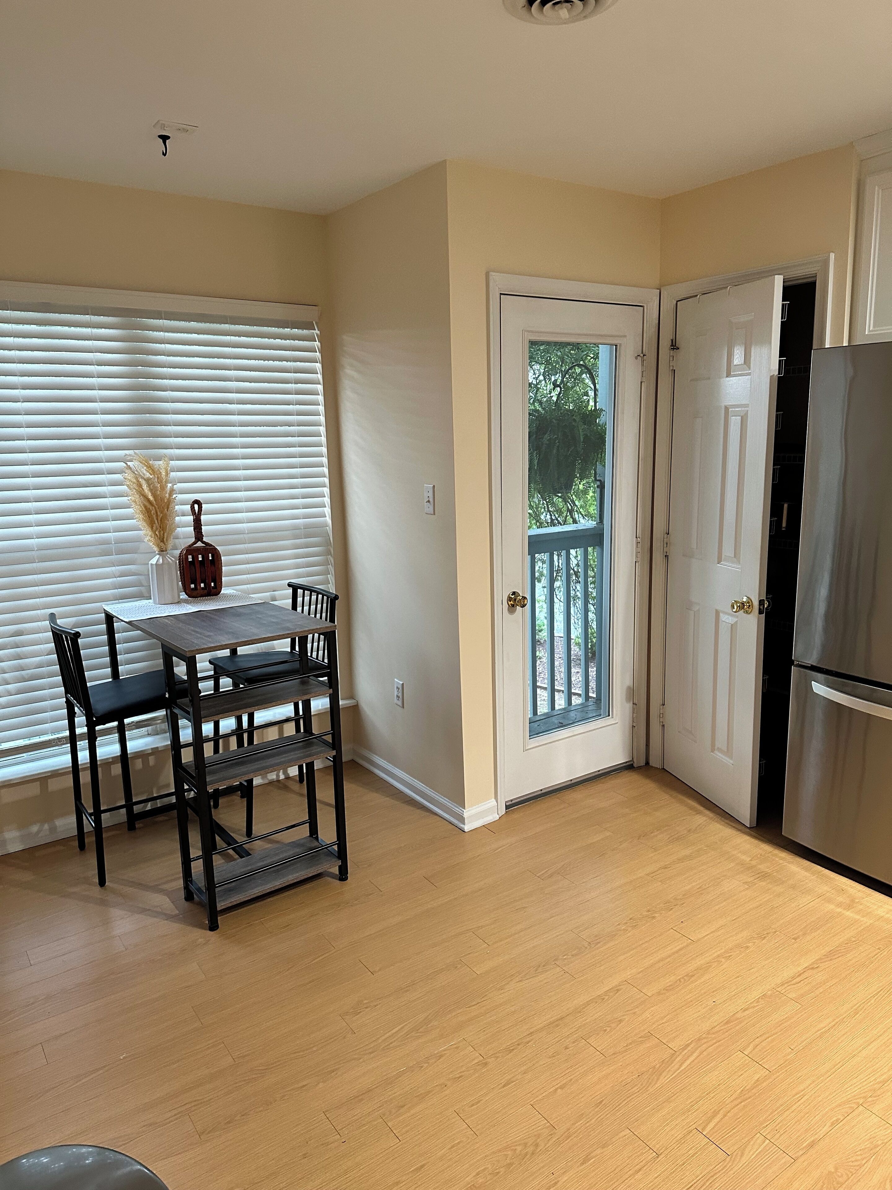 A kitchen with a dining table, chairs, a refrigerator, and a door leading outside.