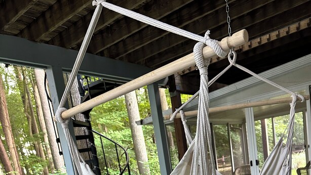 A hammock suspended from a wooden structure on a wooden deck with a view of trees and a railing.