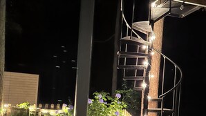 A spiral staircase with lights, surrounded by plants and a wooden deck.