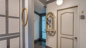 Un pasillo con una puerta blanca, un espejo en la pared y un estante decorativo con una planta.