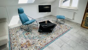 Una sala moderna con tragaluz, televisor de pantalla plana, alfombra estampada y una silla azul.