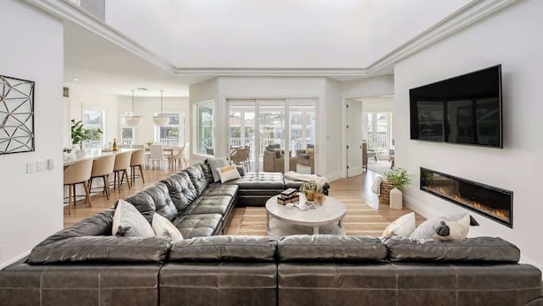 A spacious living room with a large sectional sofa, a round coffee table, and a fireplace. There is a television mounted on the wall and a ceiling fan. - Gorgeous Waterfront Home; WALK to Beach and shops (Marco Island)