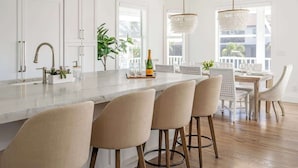 A modern kitchen with a marble island, bar stools, and a dining area with a view. - Gorgeous Waterfront Home; WALK to Beach and shops (Marco Island)