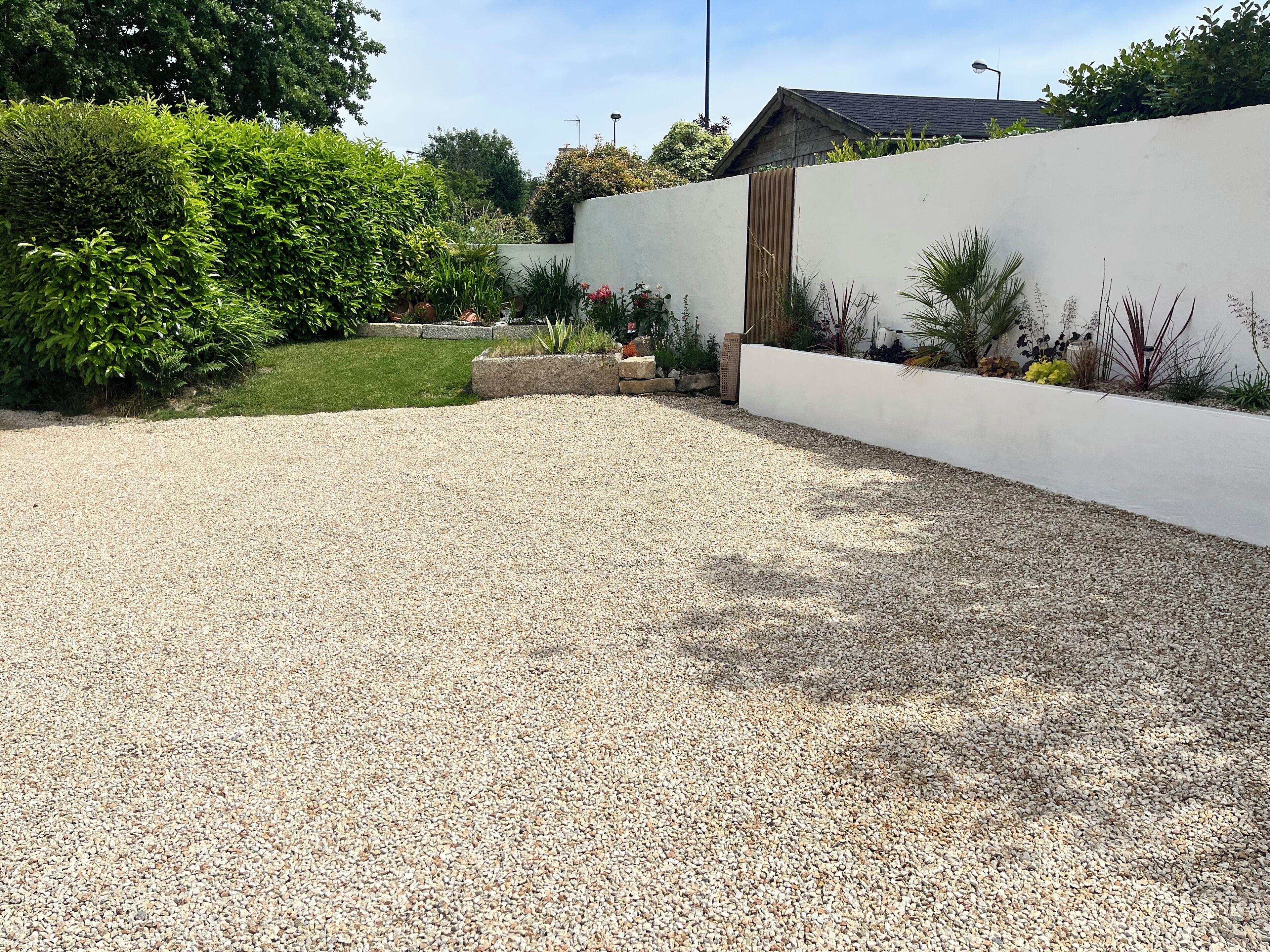 A gravel patio with a white wall and a wooden fence.