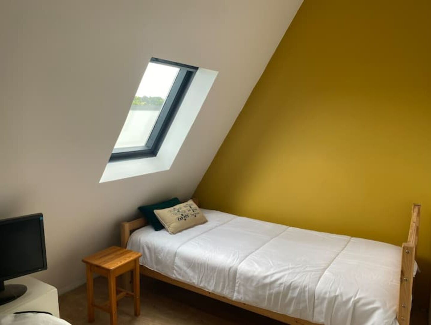 A small, single-bed room with a slanted ceiling and a skylight.
