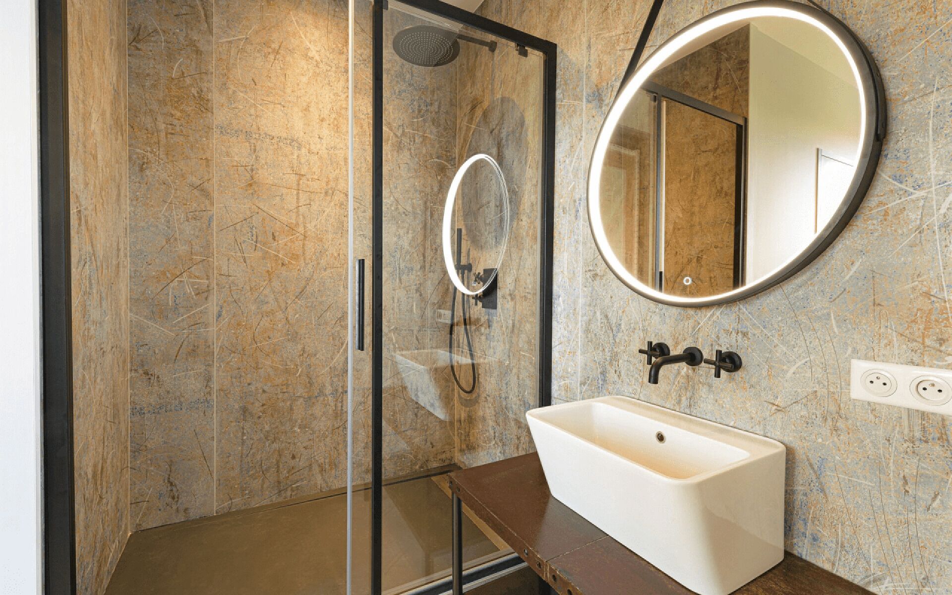 A modern bathroom with a glass-enclosed shower, a white sink, and a round mirror.