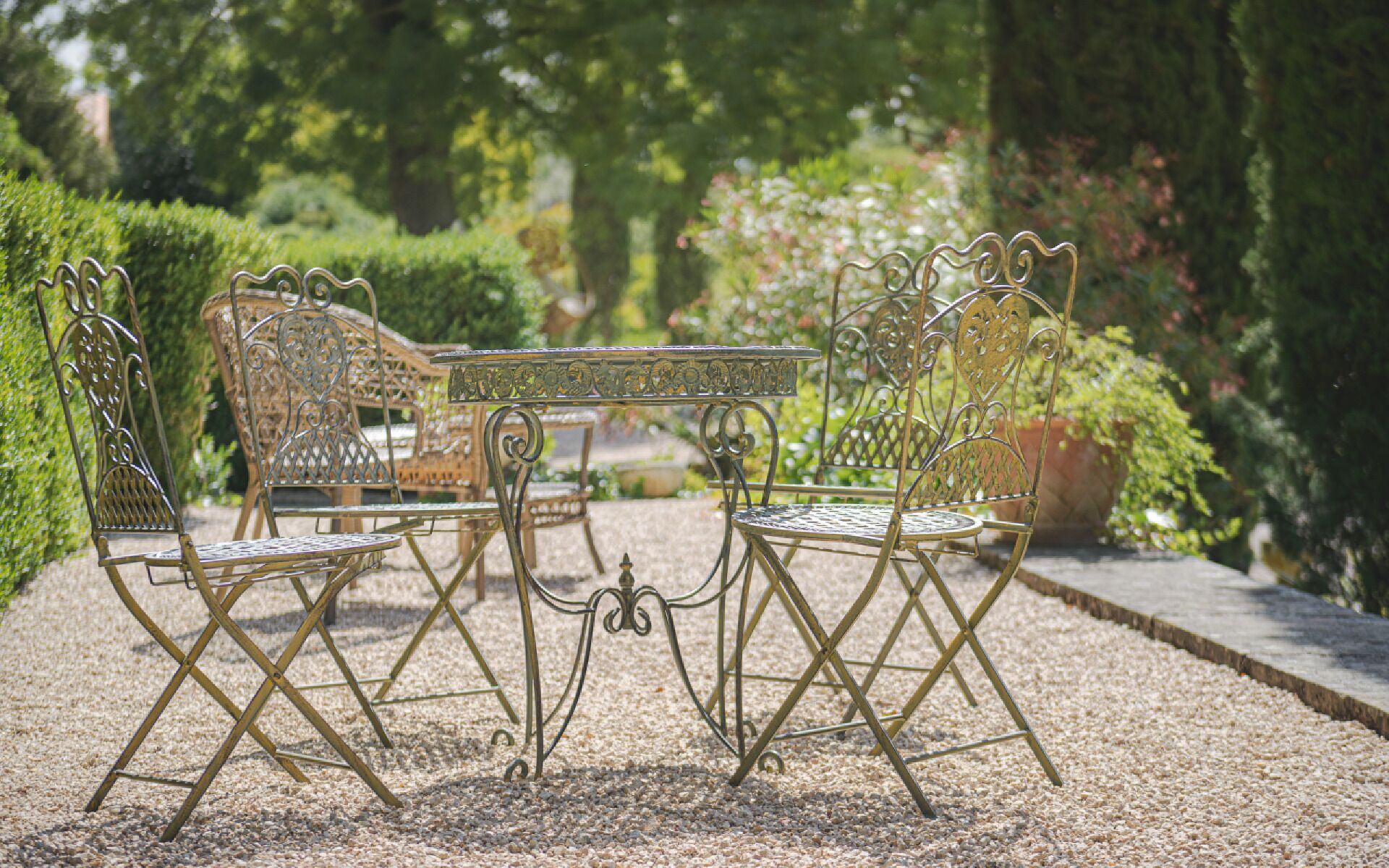 Ein Garten mit Metalltisch und -stühlen, umgeben von Grünpflanzen und einem Kiesweg.