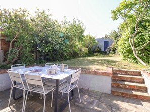 A patio with a table and chairs, surrounded by a brick wall and greenery. - Long View (Reydon)