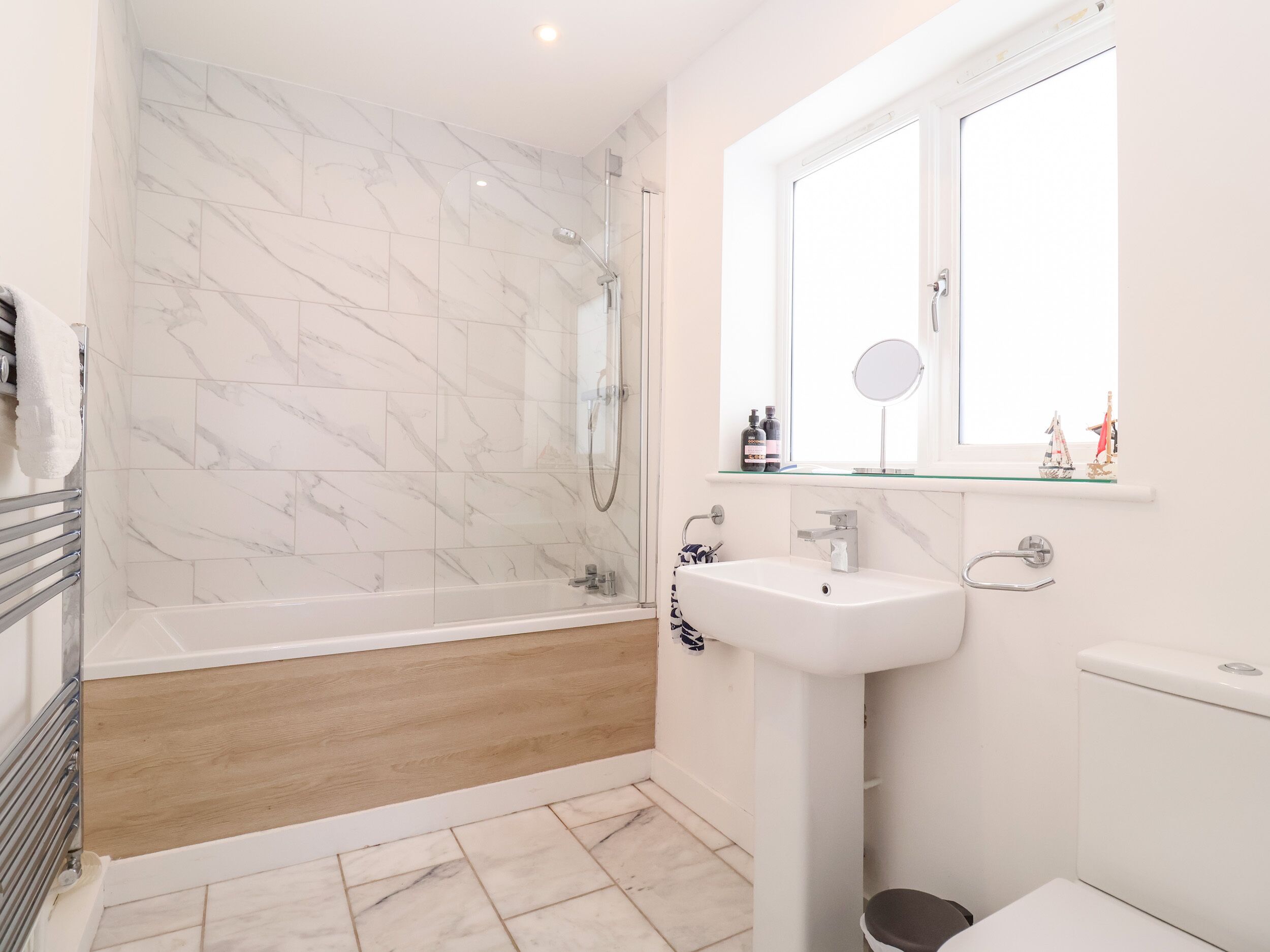 Ein modernes Badezimmer mit einer gläsernen Duschkabine, einem weißen Waschbecken und Holzboden.