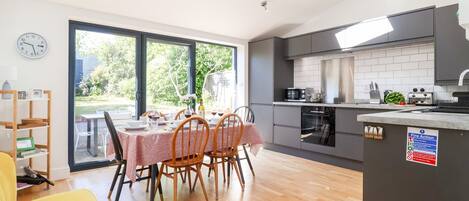 A modern kitchen with a dining area, large windows, and a view of the outdoors.
