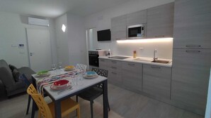 Et moderne køkken med grå skabe, en indbygget mikrobølgeovn og et spiseområde med et bord dækket til fire personer.