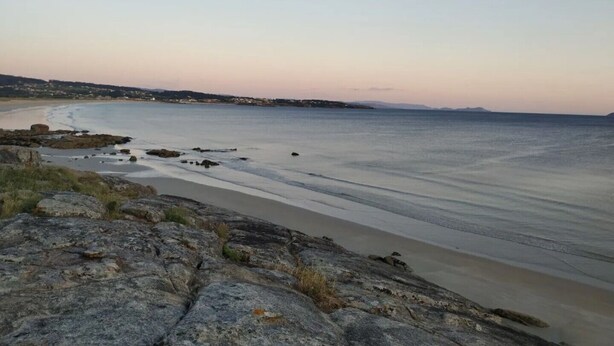 Un paysage côtier avec un premier plan rocheux, une plage de sable et une mer calme.