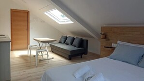 Une pièce compacte et moderne, dotée d’une lucarne, d’un lit, d’un canapé et d’un petit bureau.
