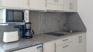 Een moderne keuken met witte kastjes, een magnetron, een koffiezetapparaat en een broodrooster.