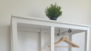 Een witte kast met drie planken, een kledingstang en een klein plantje bovenop.