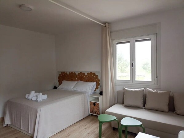 A bedroom with a bed, a sofa, two small tables, and a window with curtains.