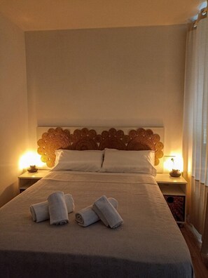 A neatly made bed with white linens and rolled towels, a wooden headboard with a floral pattern, and bedside lamps on either side.